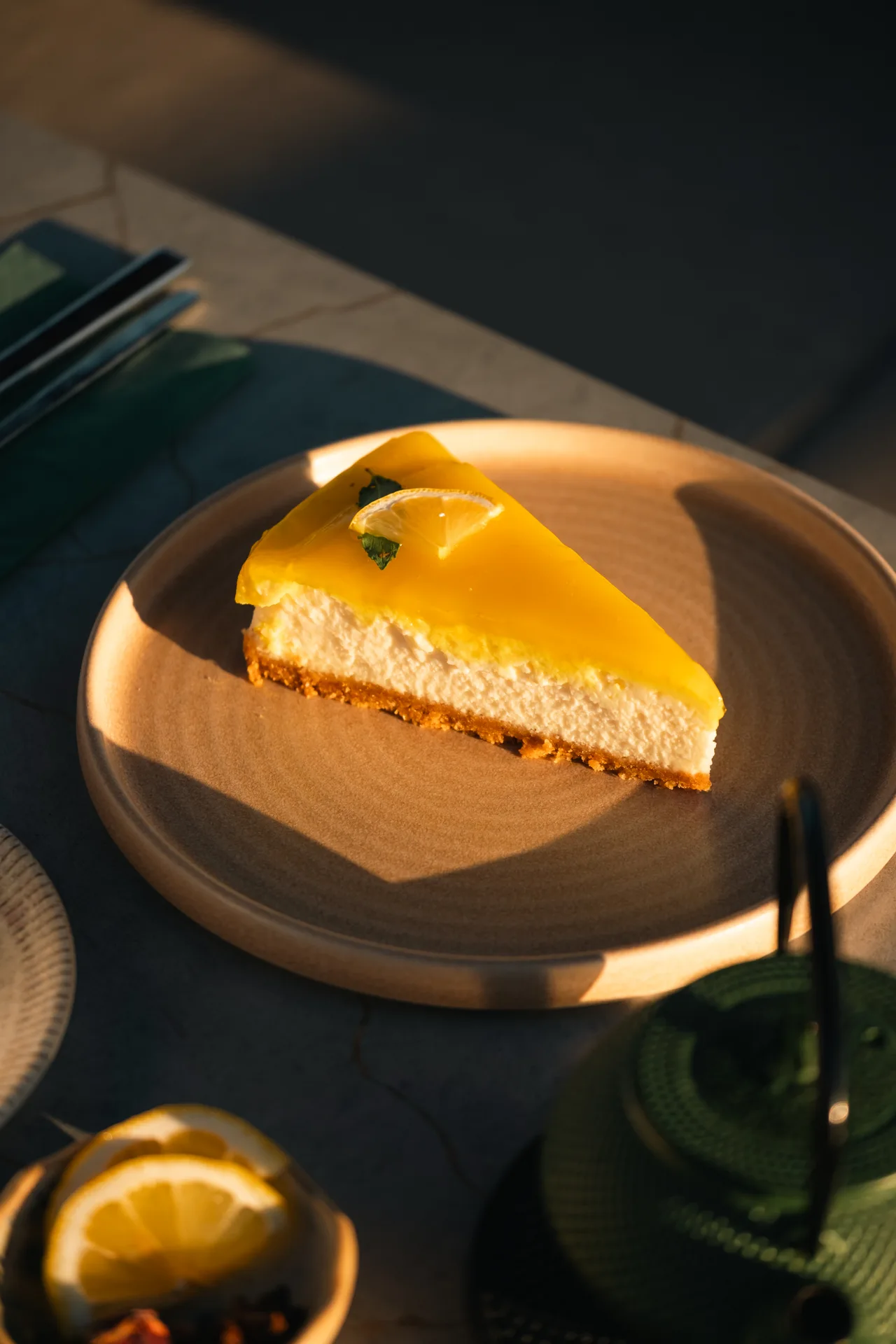 Gün ışığında sarı meyve kaplı cheesecake dilimi ve yeşil şişe.